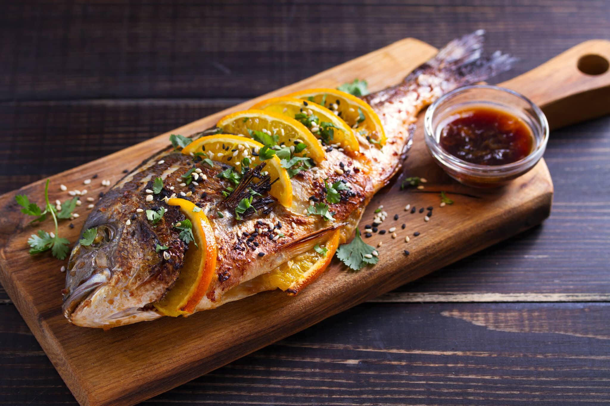 Orange ginger sea bream fish, sprinkled with sesame seeds and cilantro on serving board Soy orange sauce